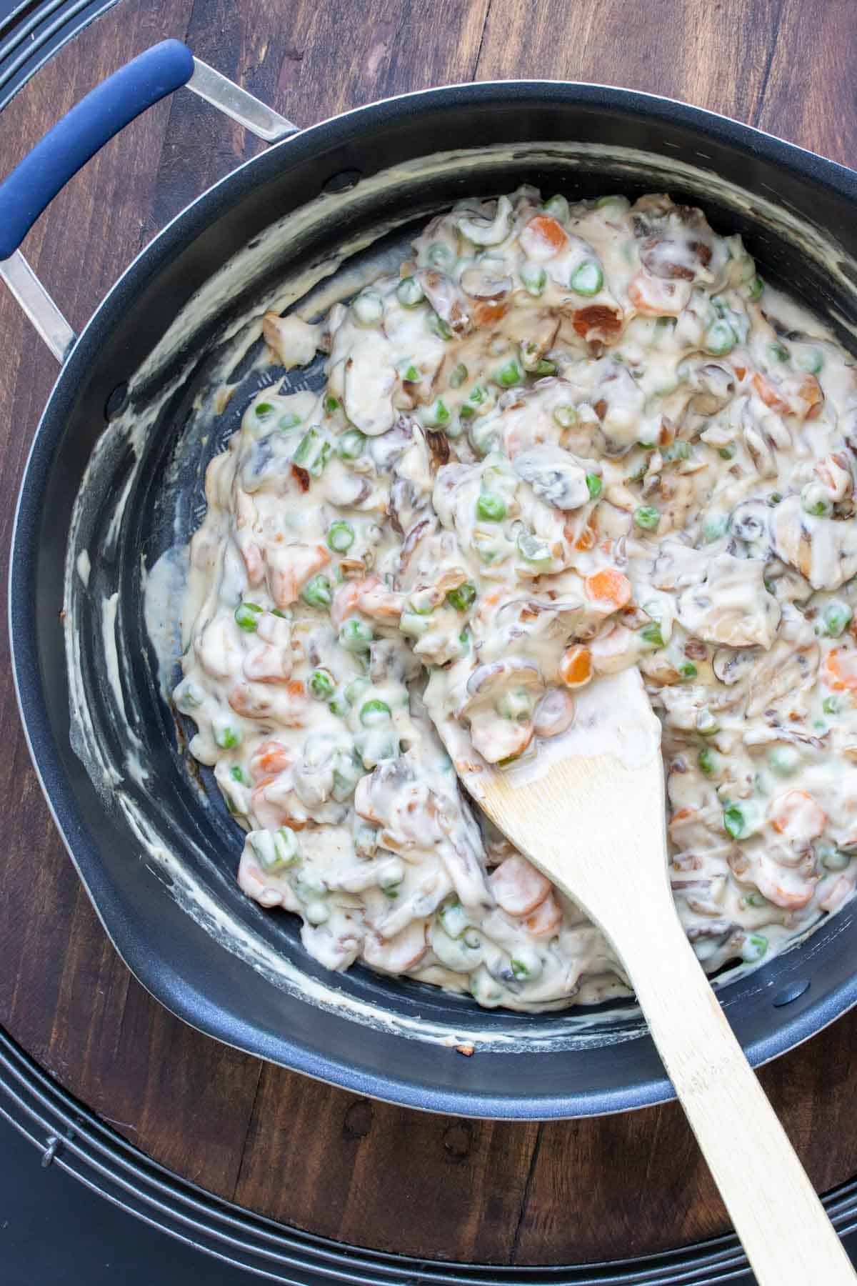 Wooden spoon mixing a creamy sauce into some veggies in a pan.