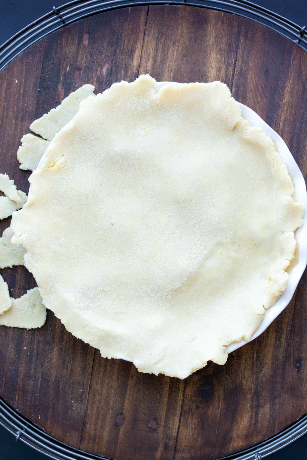 Top view of a raw pie crust being put over the top of a pie.