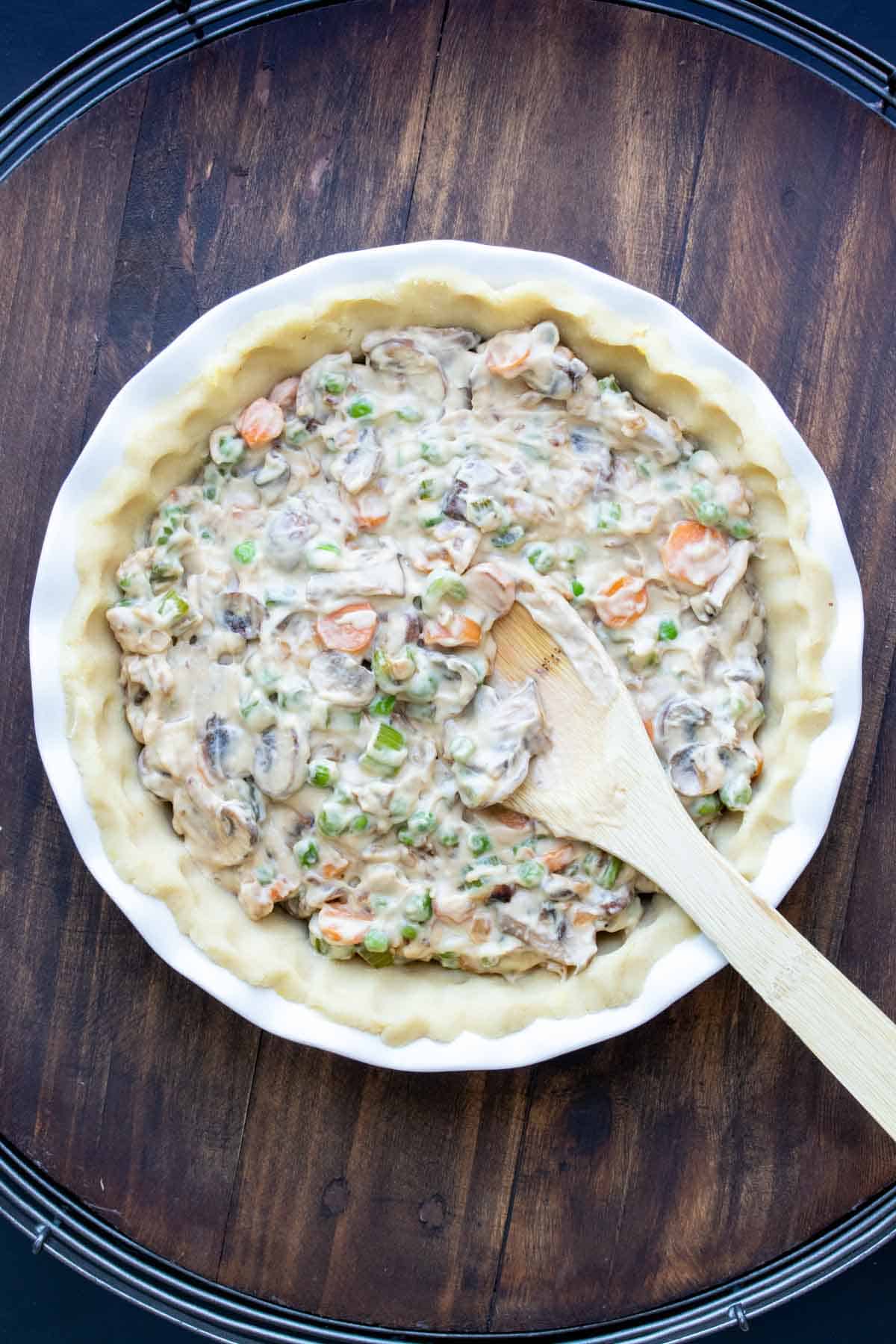 Wooden spoon putting pot pie filling into a pie crust