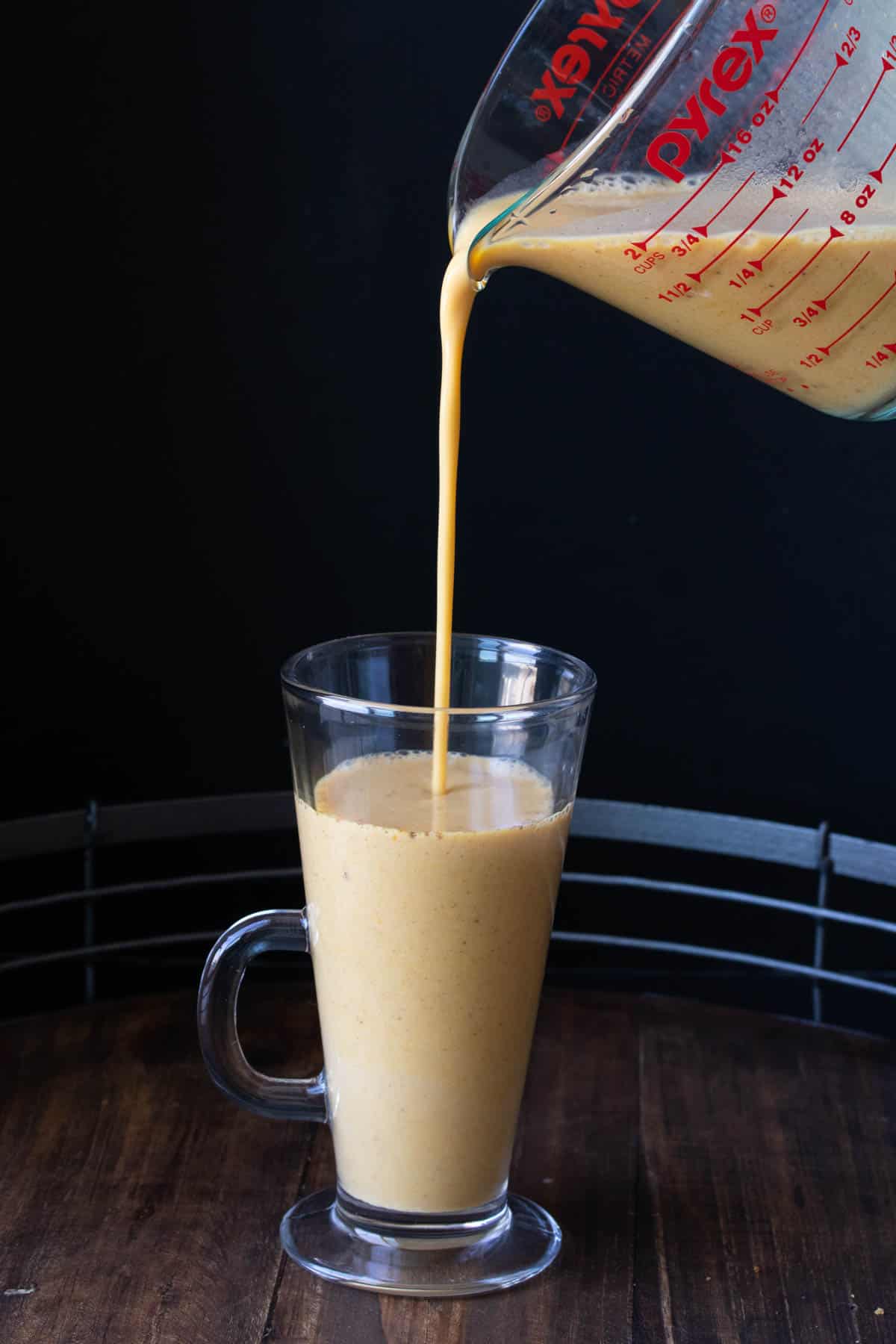 Glass measuring cup pouring pumpkin spice latte into a tall glass