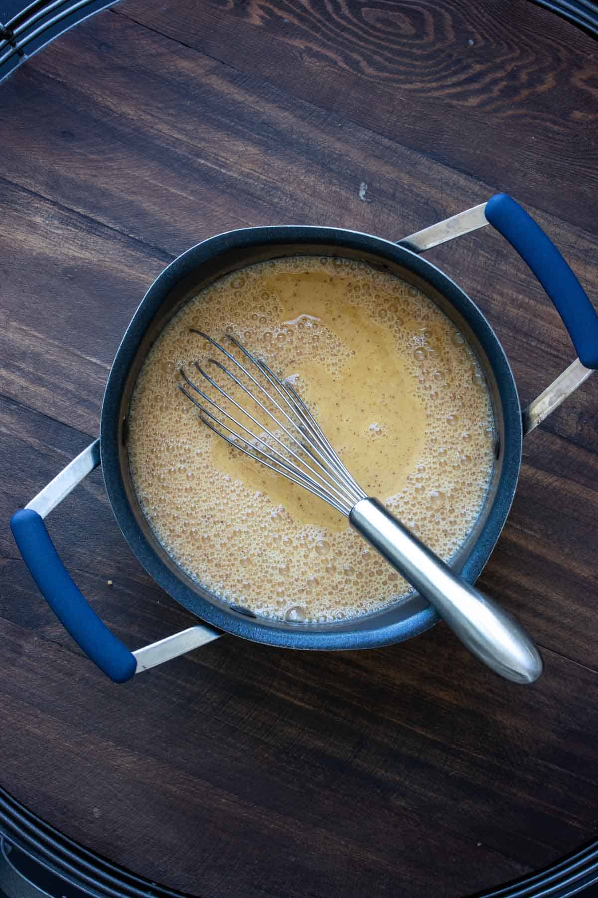 Whisk mixing ingredients for a pumpkin spice latter in a pot