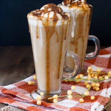 Two tall glasses on an orange checkered towel filled with a pumpkin spice latte drink