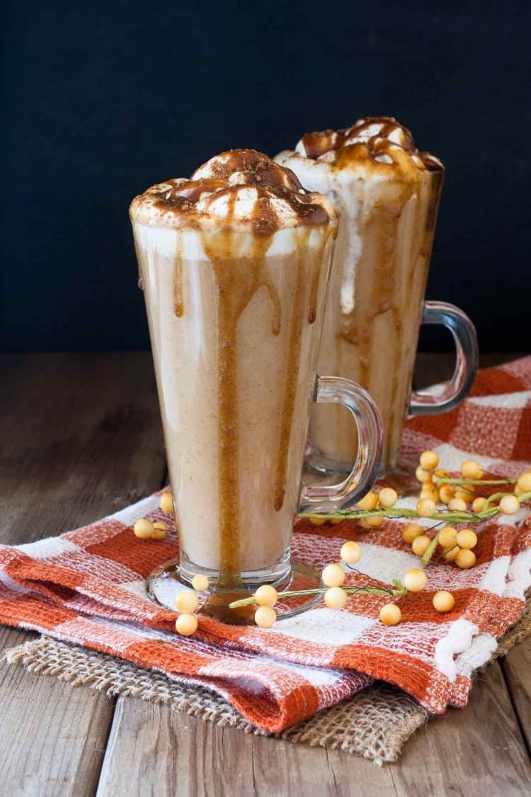 Two tall glasses on an orange checkered towel filled with a pumpkin spice latte drink