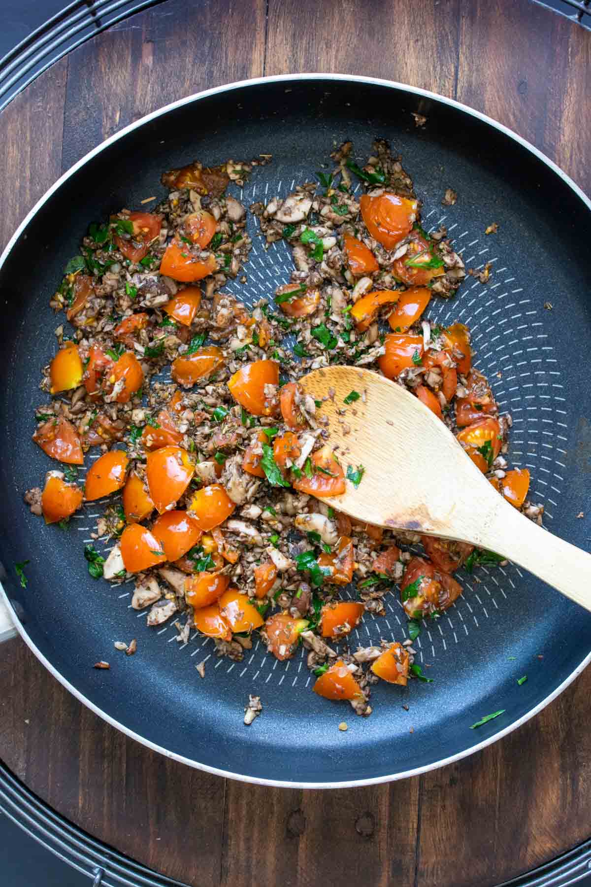 Wooden spoon sautéing tomatoes, mushrooms and herbs