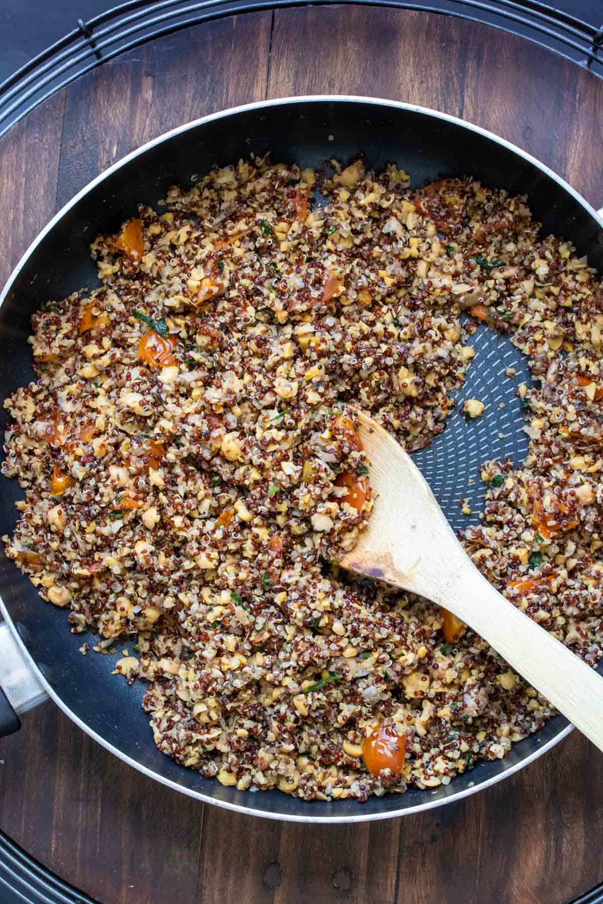 Spoon mixing quinoa with chopped mushrooms and chickpeas in a pan