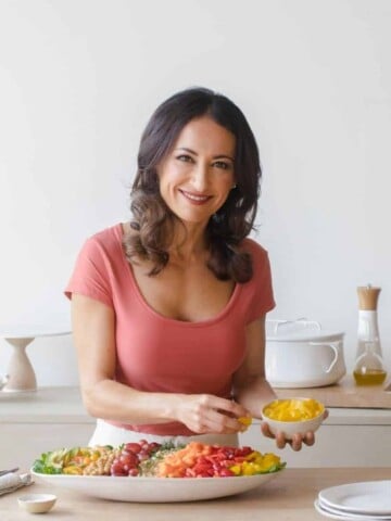 A woman in a pink shirt building a salad in a tan and white kitchen