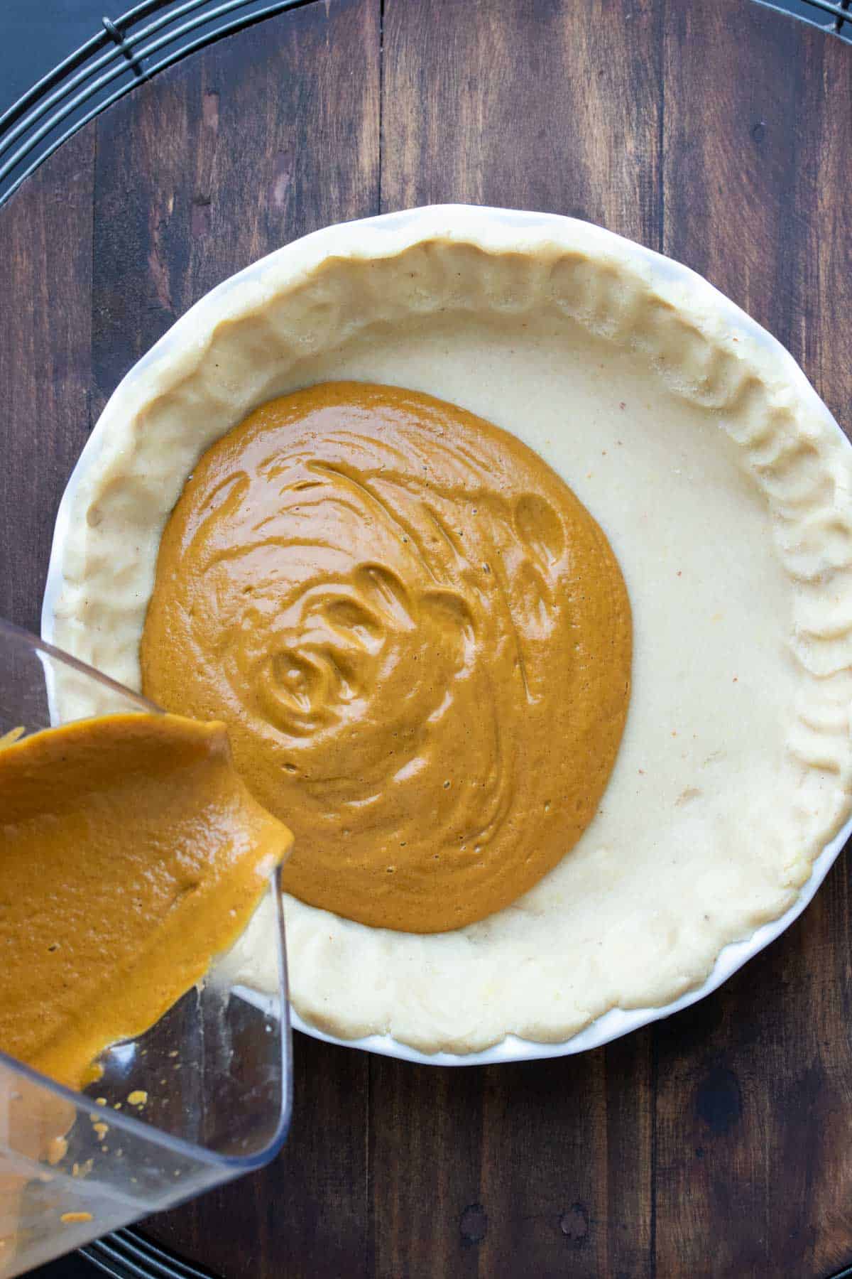 Pumpkin pie filling being poured into a pie crust