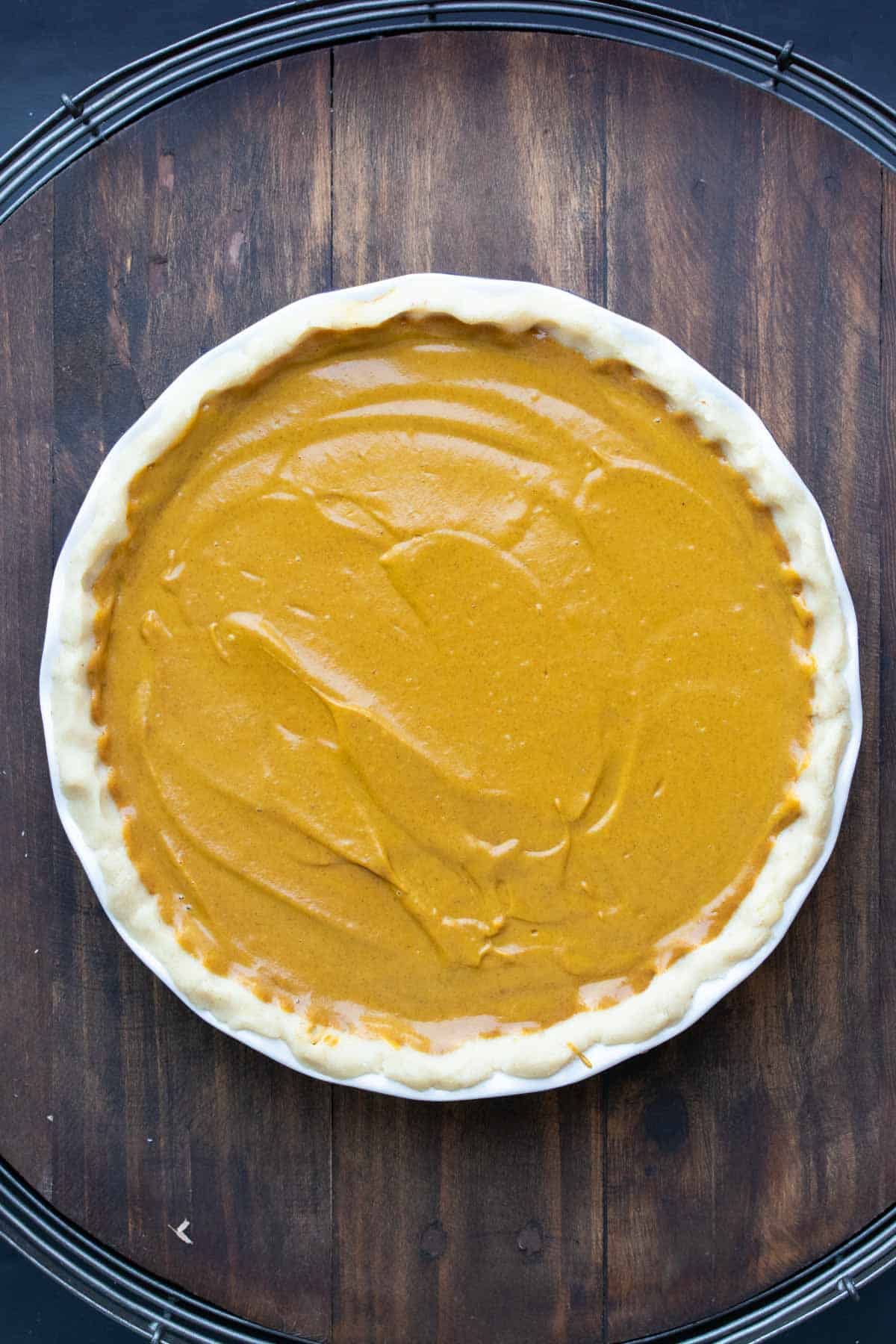 A raw pumpkin pie in a pie crust on a wooden surface.