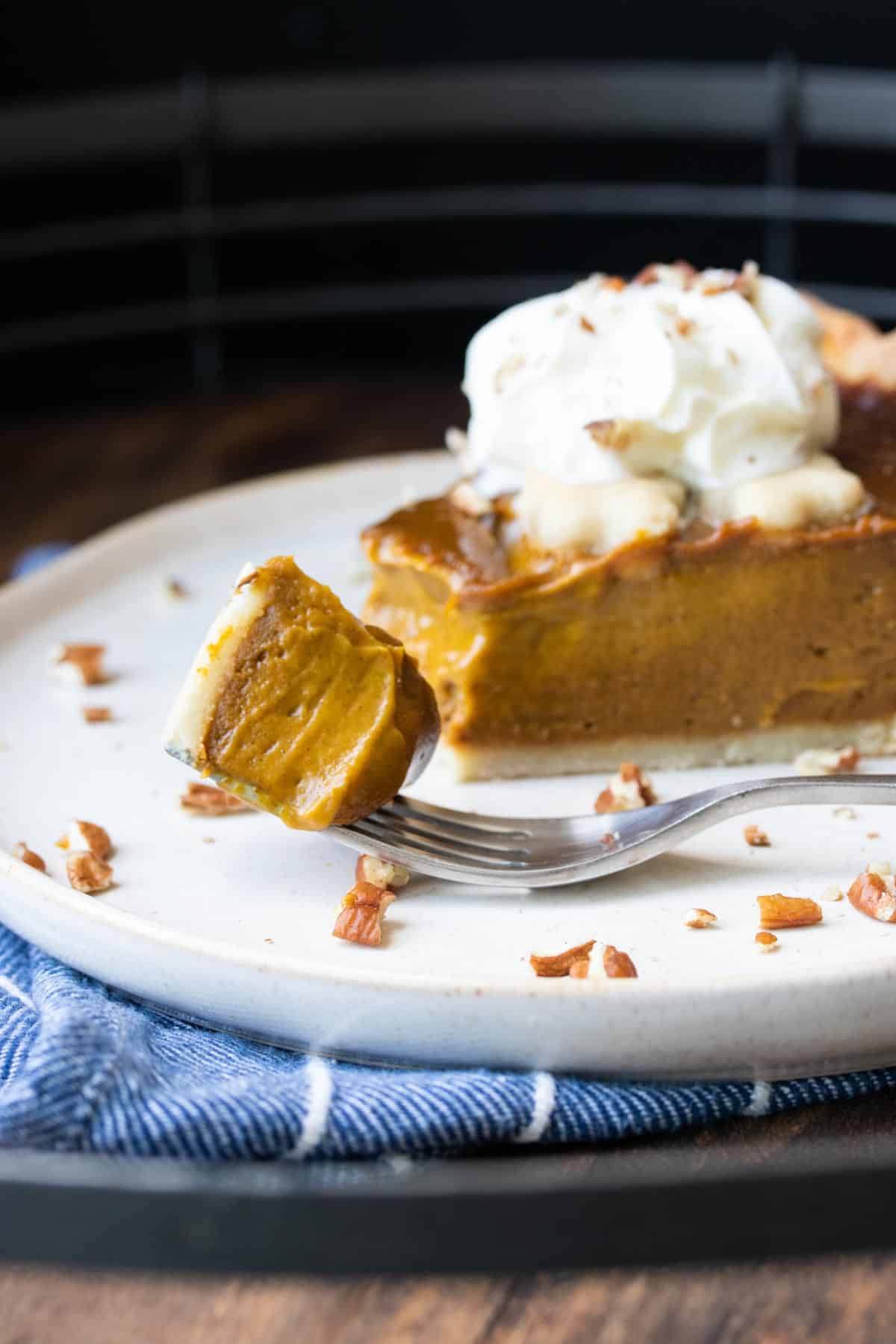 Front view of a fork with a bite of pumpkin pie on a plate.