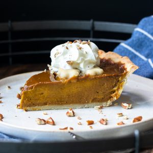 A slice of pumpkin pie on a plate topped with whipped cream.
