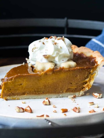 A slice of pumpkin pie on a plate topped with whipped cream.