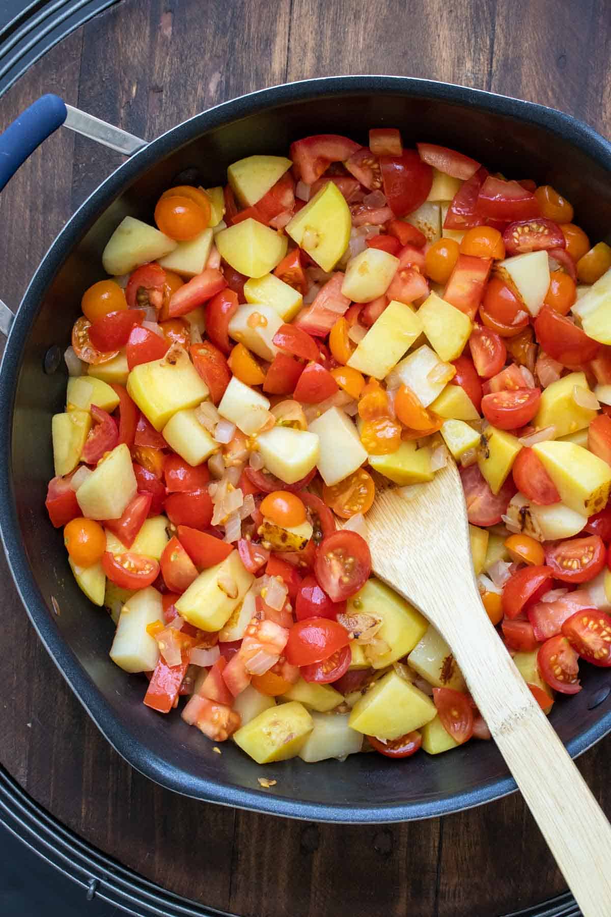 Potatoes and tomatoes being cooked in a pan