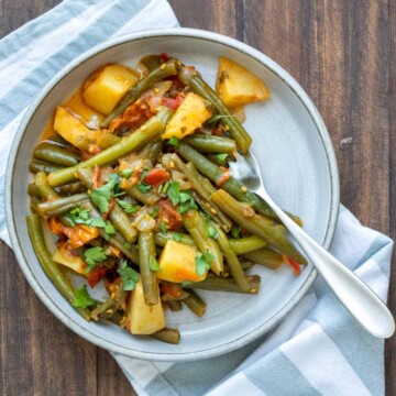 Sautéed green beans with potatoes and tomatoes on a grey plate