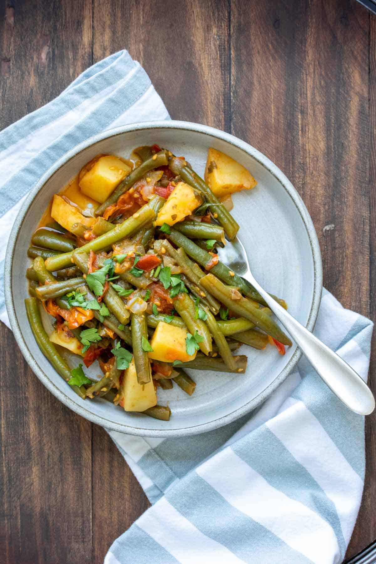 Sautéed green beans with potatoes and tomatoes on a grey plate