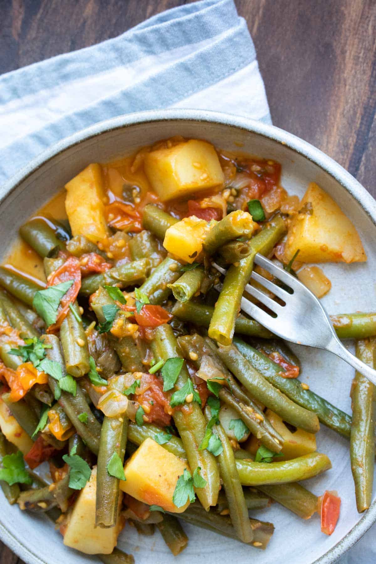 Fork getting a bite of cooked green beans and tomatoes with tomato mix