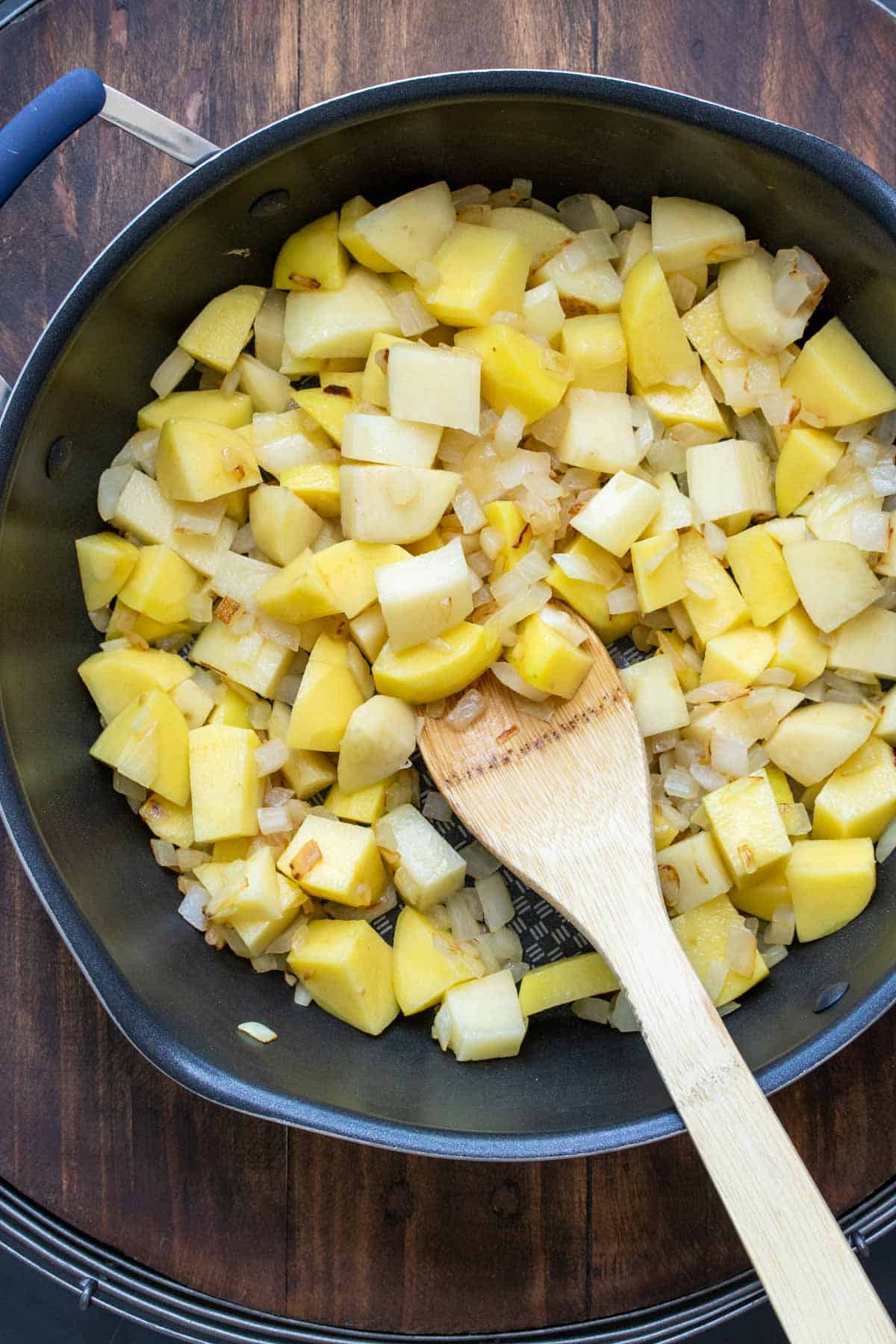 Wooden spoon mixing cut potatoes in a pan