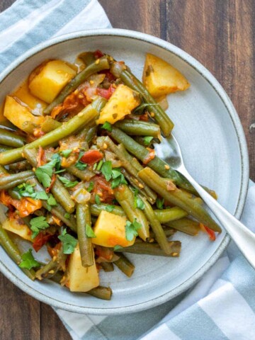 Sautéed green beans and potatoes in a tomato sauce on a grey plate