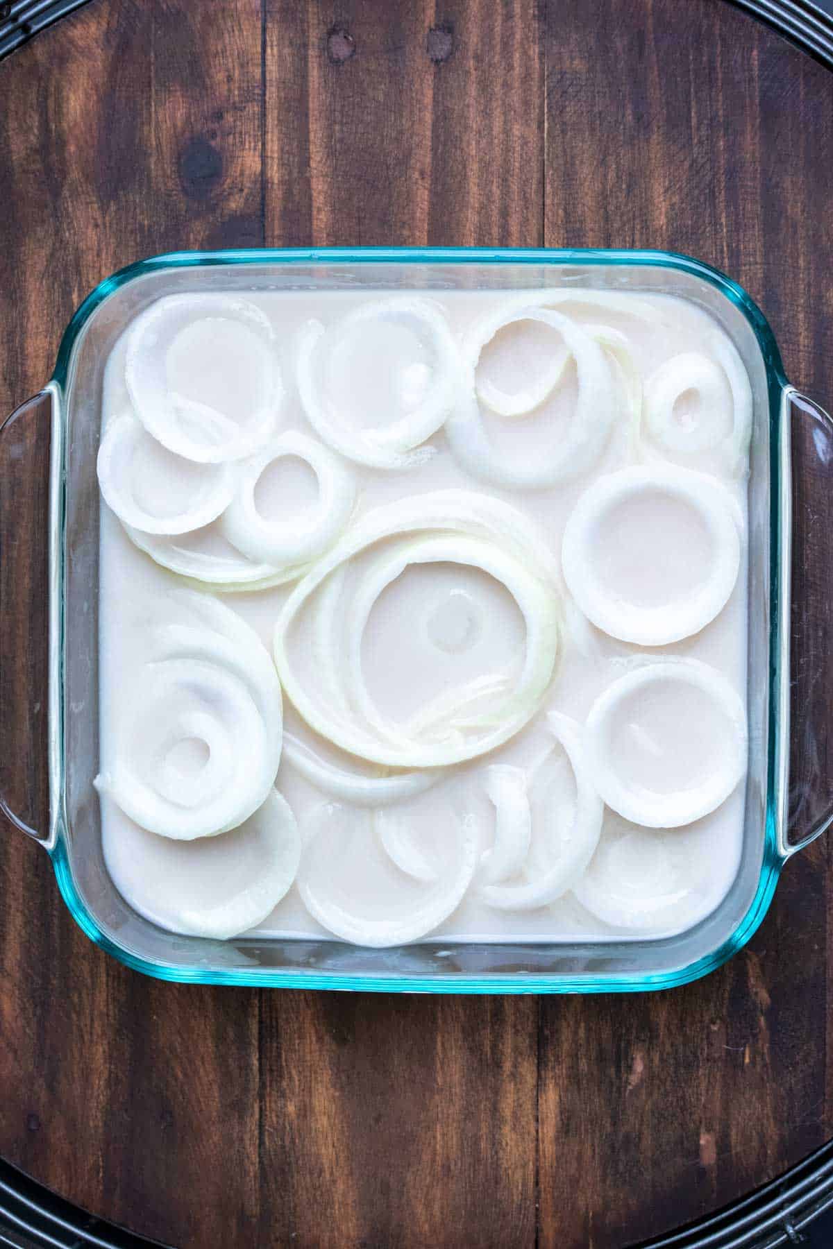 Slices of white onion soaking in a pan of milk