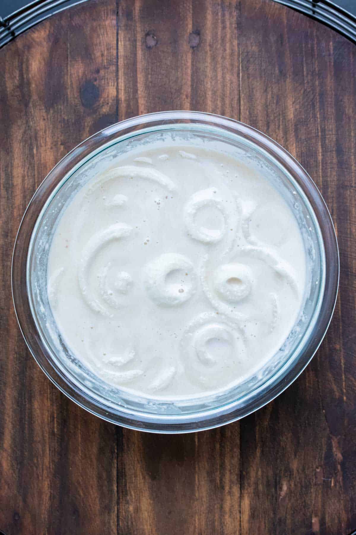 Slices of white onion in a bowl of batter