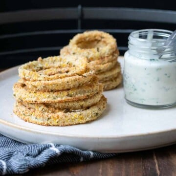 A pile of onion rings on a plate next to dip