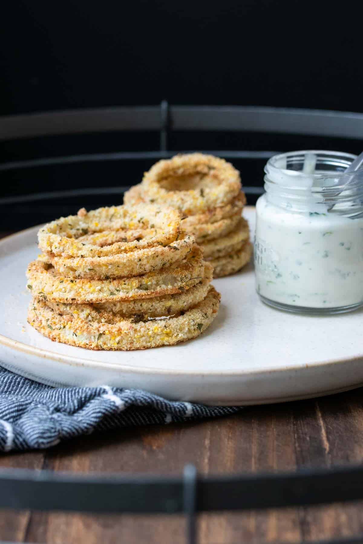 A pile of onion rings on a plate next to dip