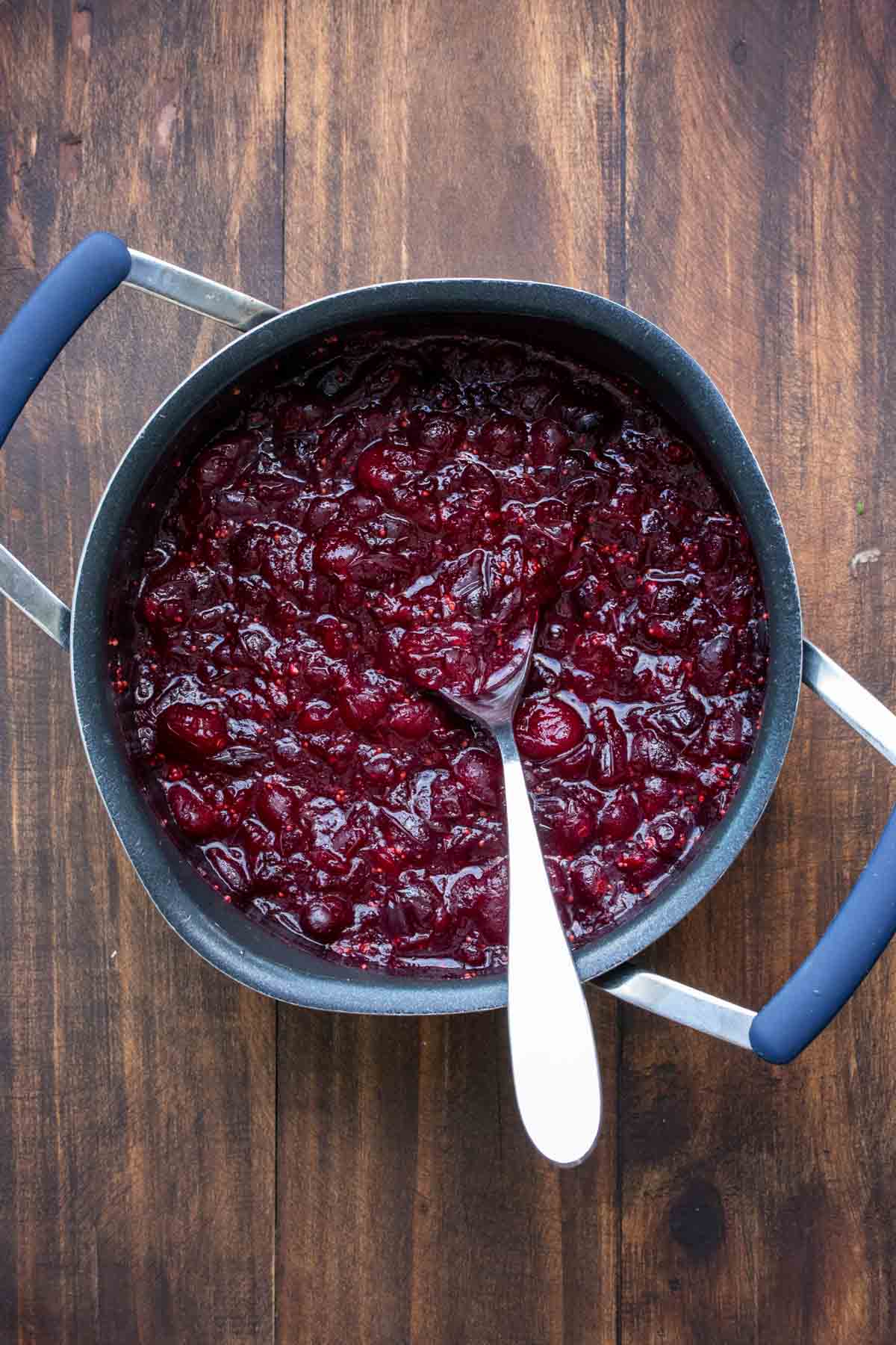 A spoon stirring cranberry sauce cooking in a pot