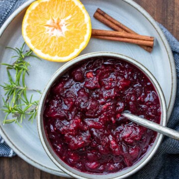 A bowl of cranberry sauce sitting on a plate with an orange and cinnamon stick