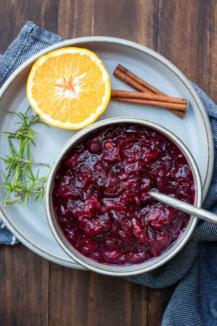 A bowl of cranberry sauce sitting on a plate with an orange and cinnamon stick
