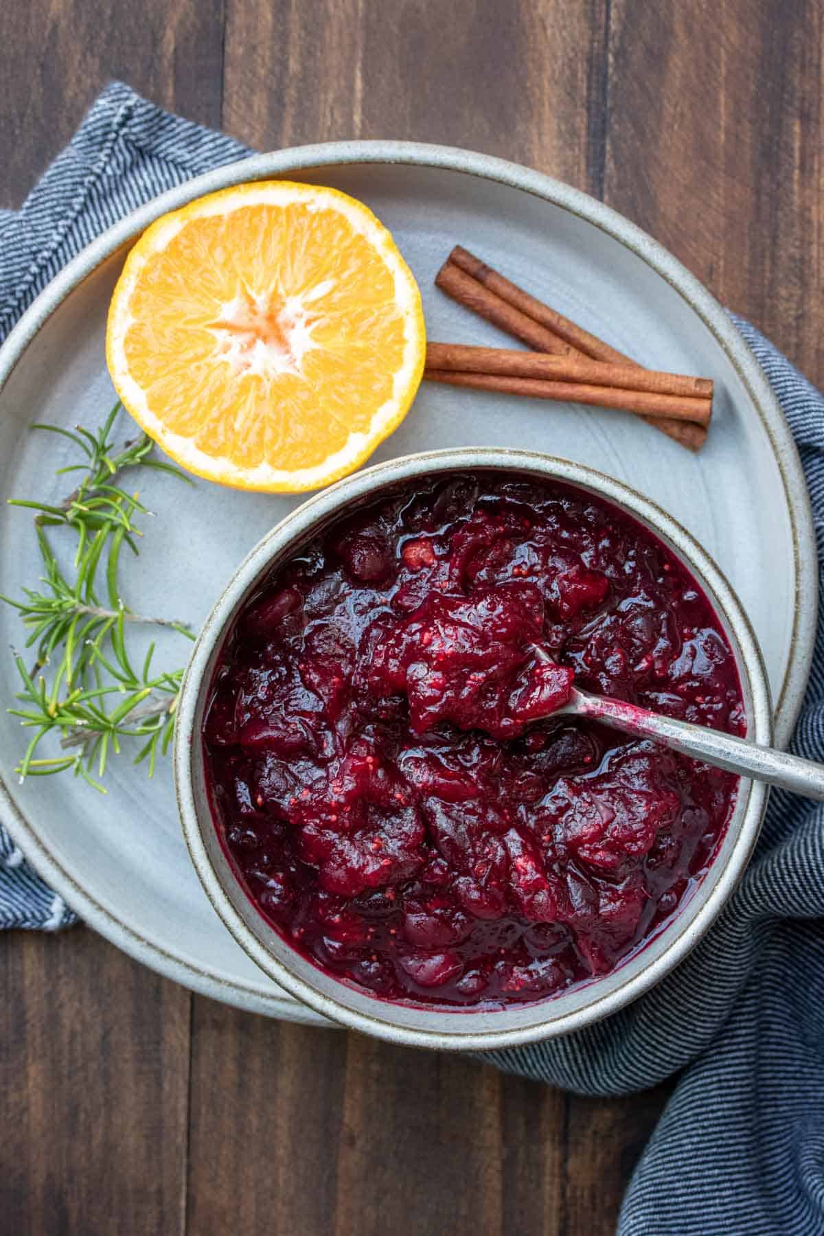 A spoon getting a scoop of cranberry sauce from a grey bowl