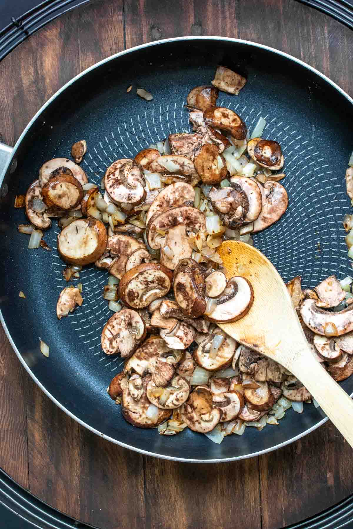 Wooden spoon stirring mushrooms in a frying pan