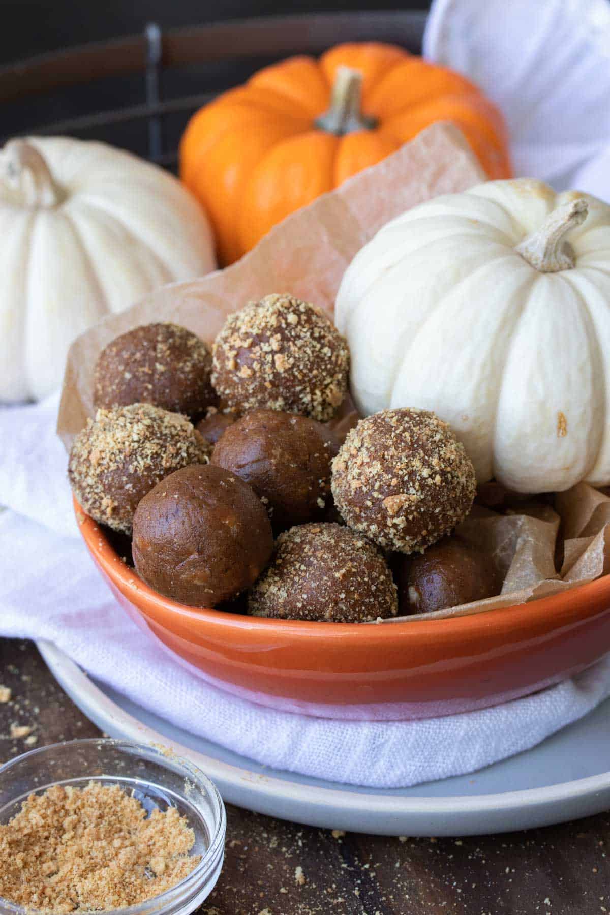 Orange bowl with a pile of pumpkin energy balls and some covered in graham crackers