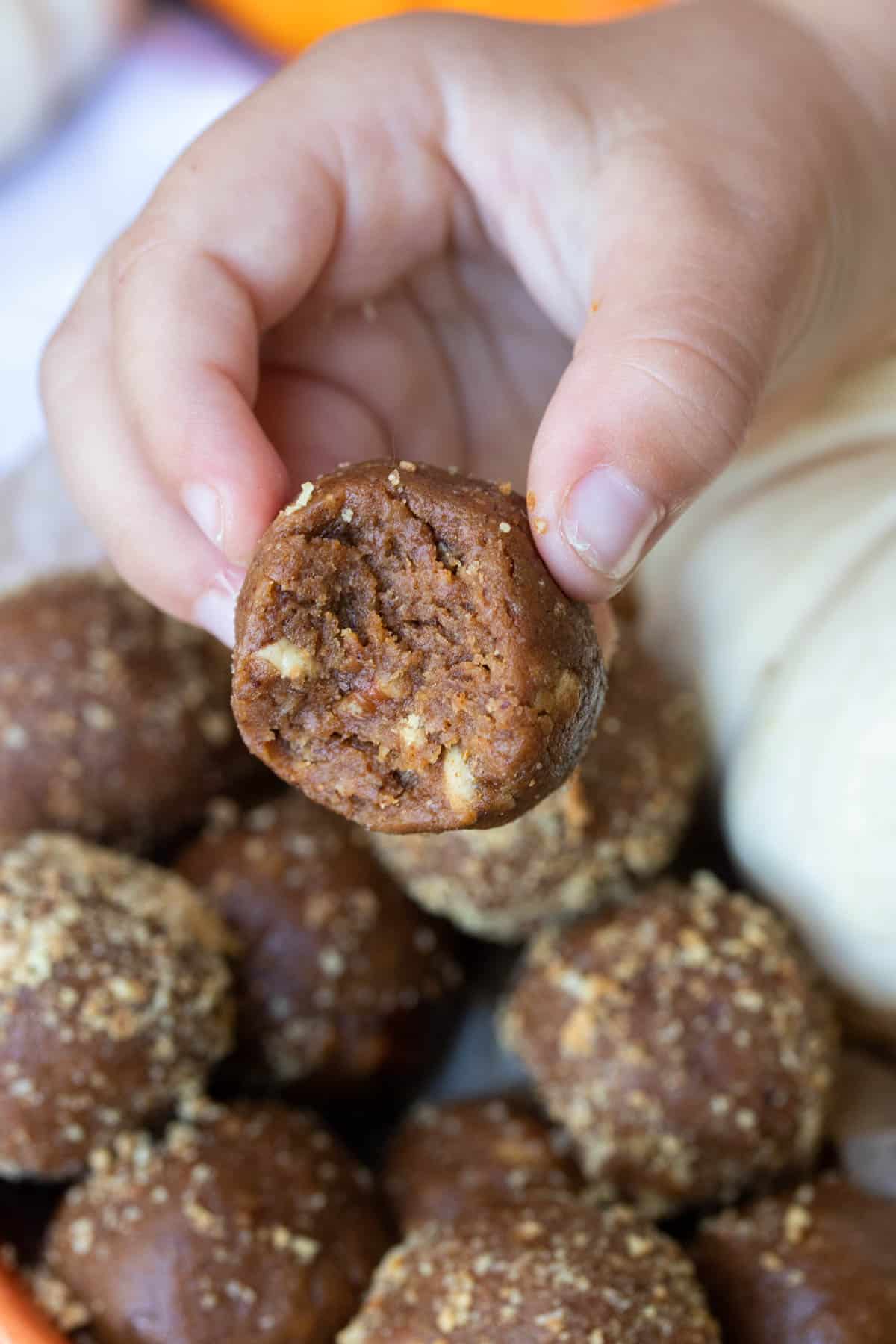 Hand holding a pumpkin pie energy ball with a bite out