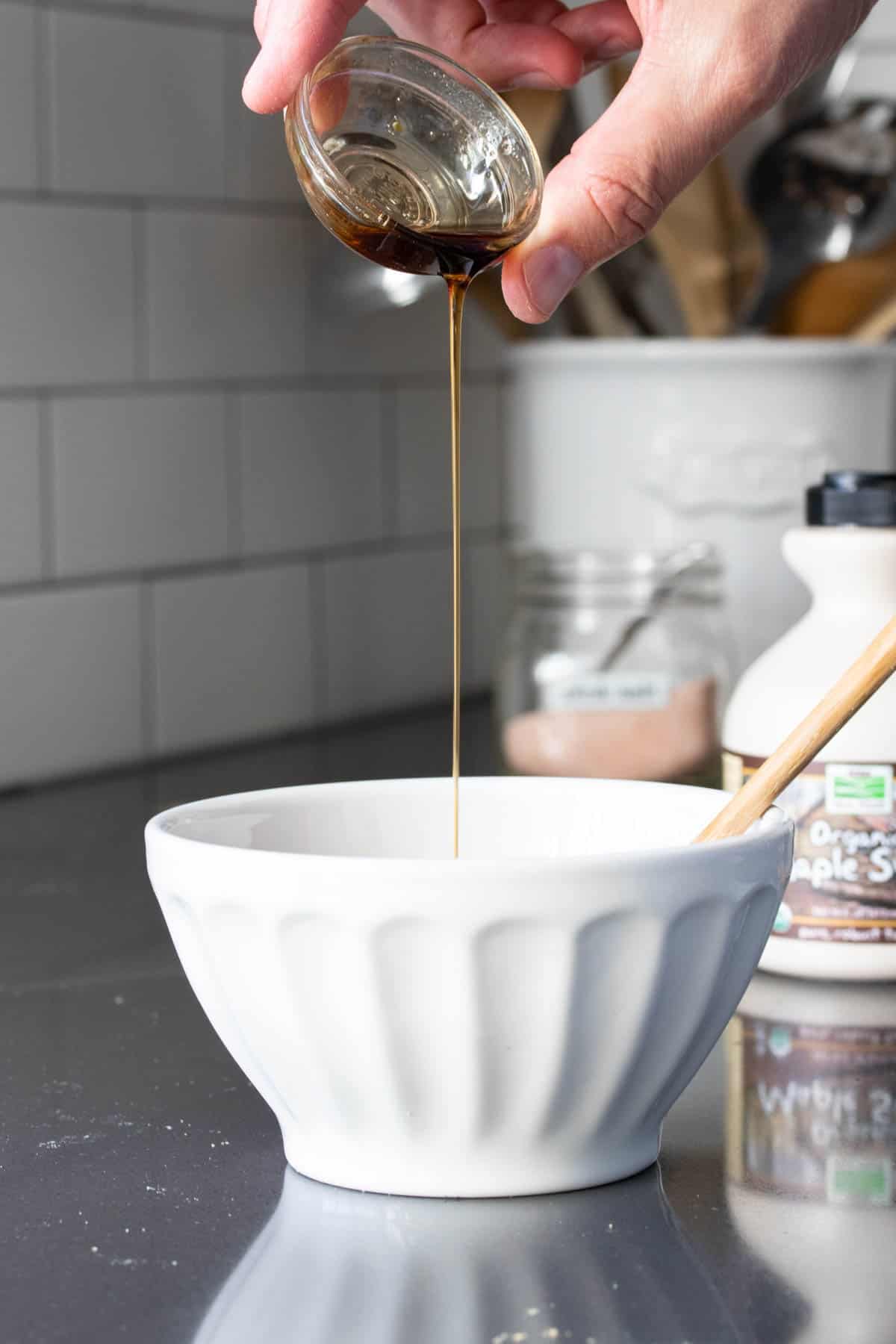 Hand drizzling maple syrup into a white bowl