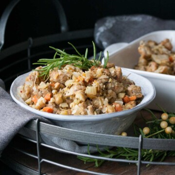 Thanksgiving stuffing with a sprig of rosemary in a white bowl on a wooden tray