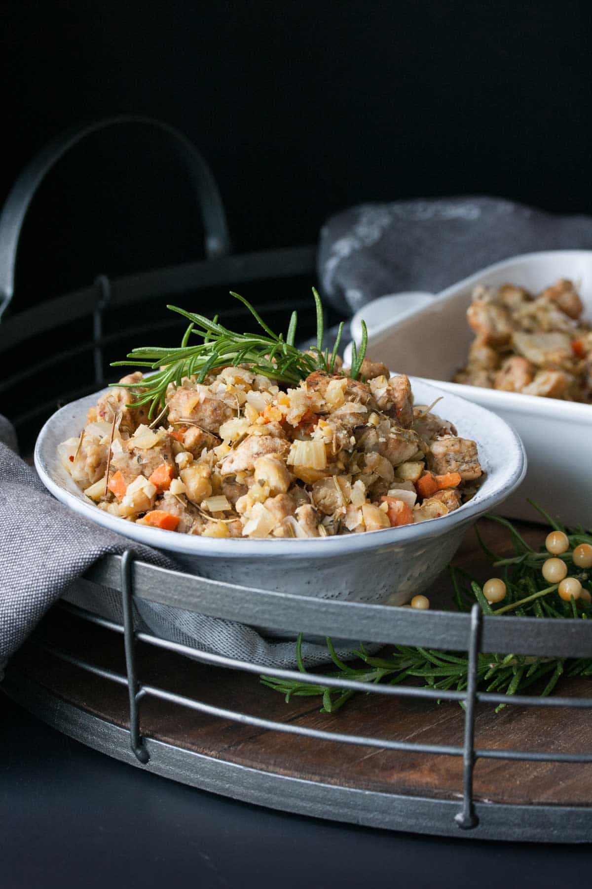 Thanksgiving stuffing with a sprig of rosemary in a white bowl on a wooden tray