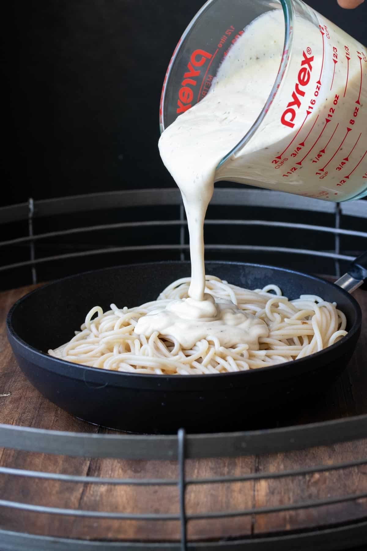 Skillet filled with fettuccini and Alfredo sauce being poured over the top