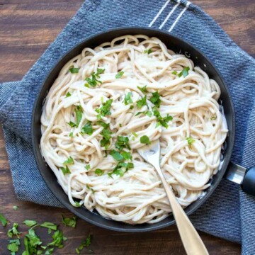 Top view of a black skillet filled with Alfredo pasta and sprinkled with parsley