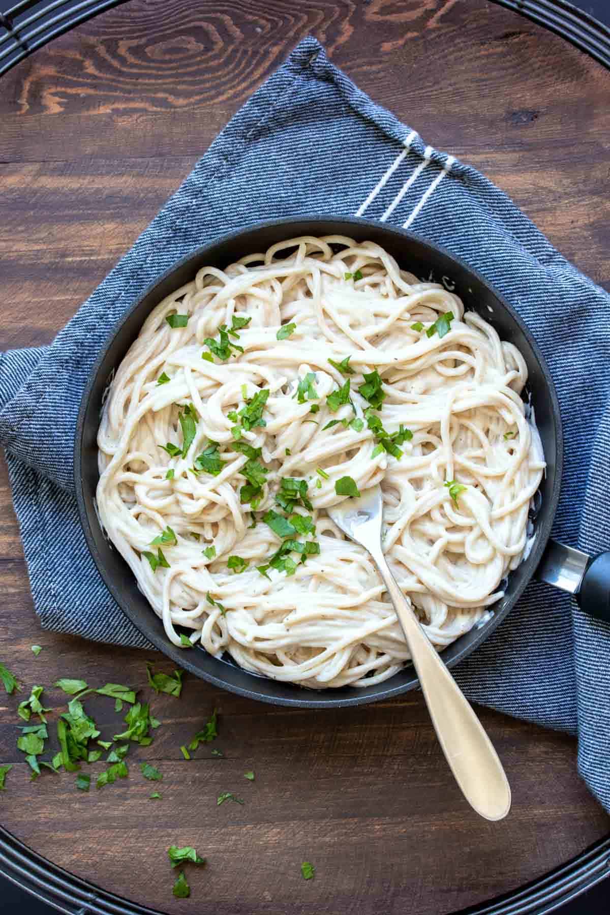 Top view of a black skillet filled with Alfredo pasta and sprinkled with parsley