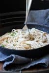 Fork twirling Alfredo covered fettuccini noodles in a black skillet