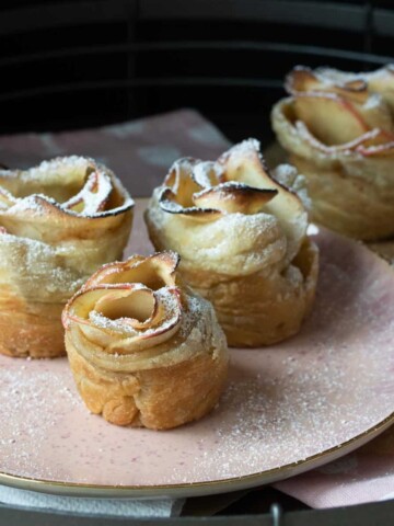 Pink plate dusted with powdered sugar with apple roses on it