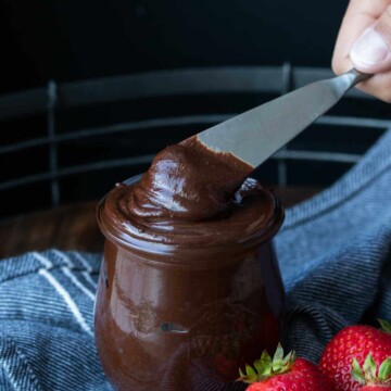 A glass jar full of Nutella and a knife getting a scoop out