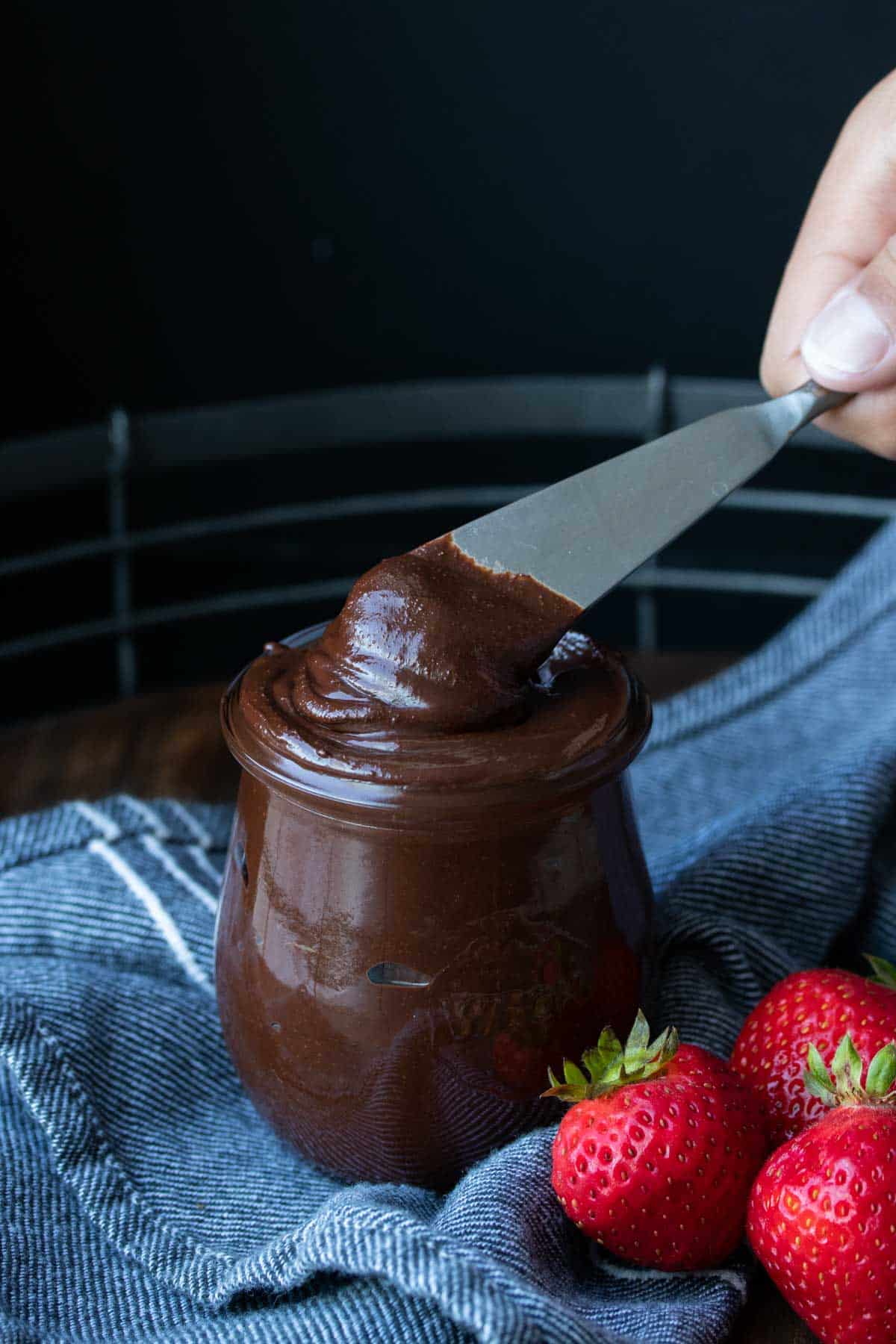 A glass jar full of Nutella and a knife getting a scoop out