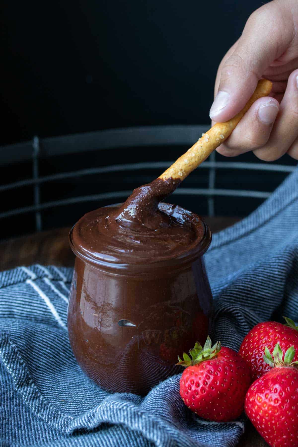 A pretzel being dipped in a jar of Nutella