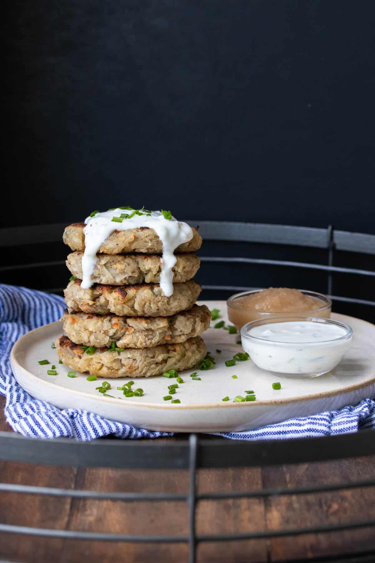 Stack of potato pancakes on a cream plate with dippers next to it