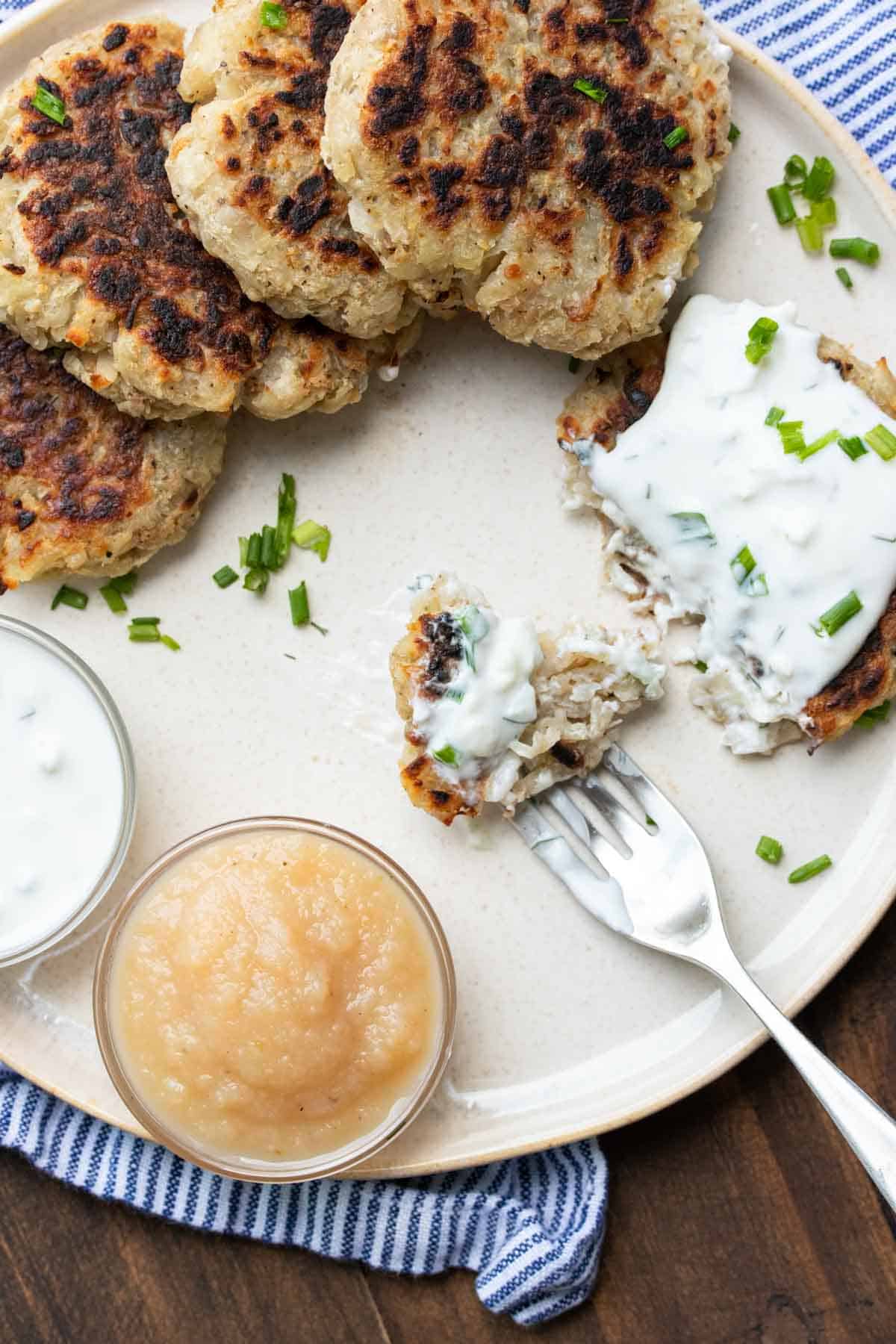 A fork getting a bite from a potato pancake on a cream plate