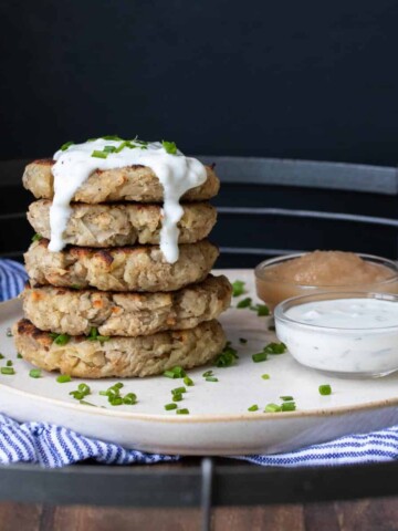 Five latkes piled up next to bowls of sour cream and apple sauce