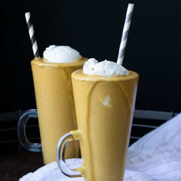 Two glass jars with pumpkin pie milkshakes topped with whipped cream