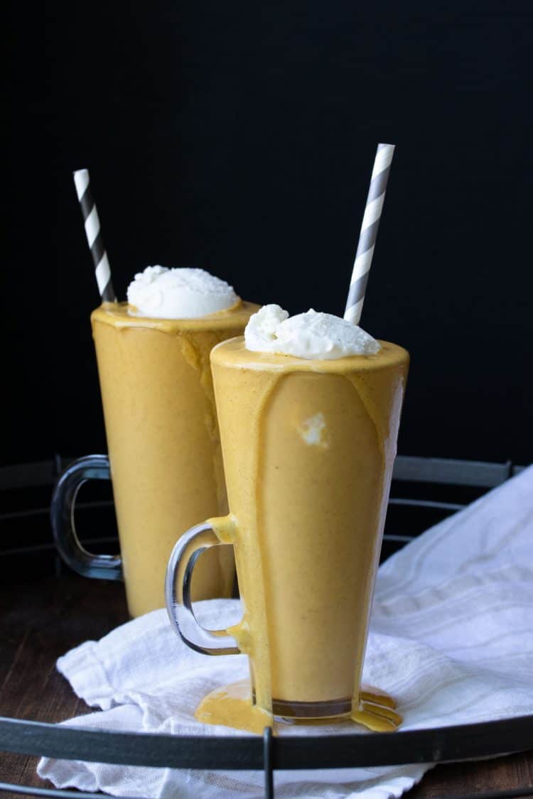 Two glass jars with pumpkin pie milkshakes topped with whipped cream
