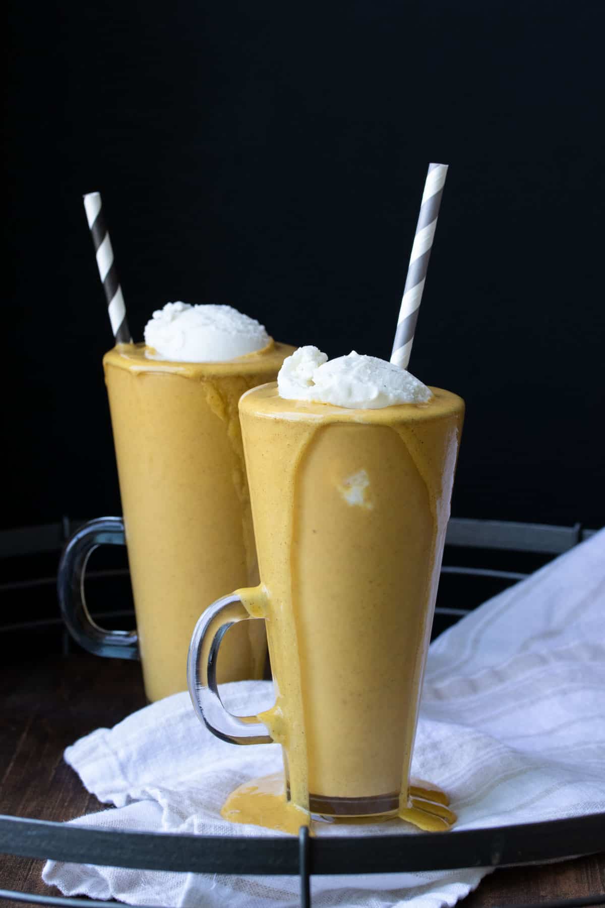 Two glass jars with pumpkin pie milkshakes topped with whipped cream