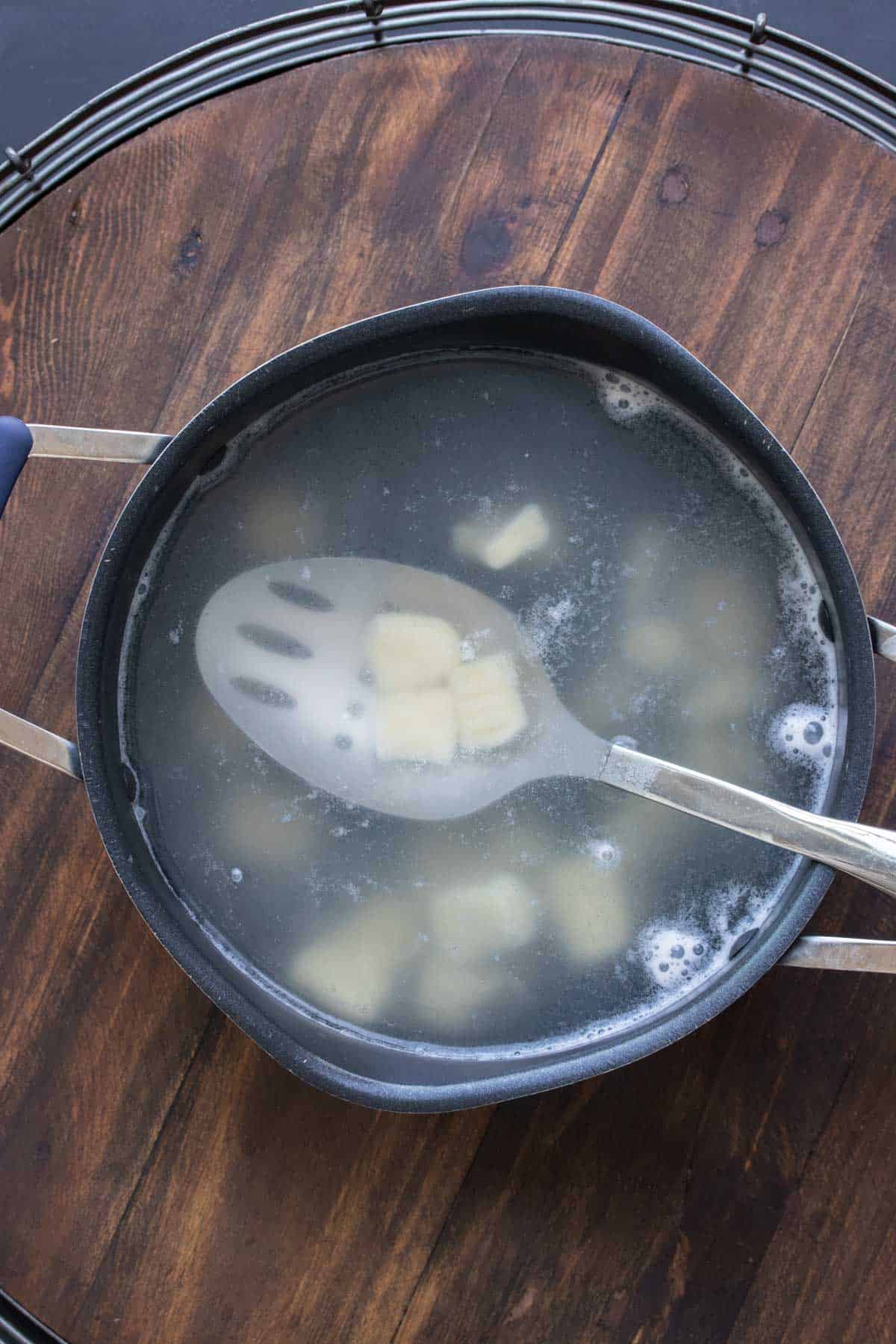 Slotted spoon getting cooked gnocchi out of a pot of water